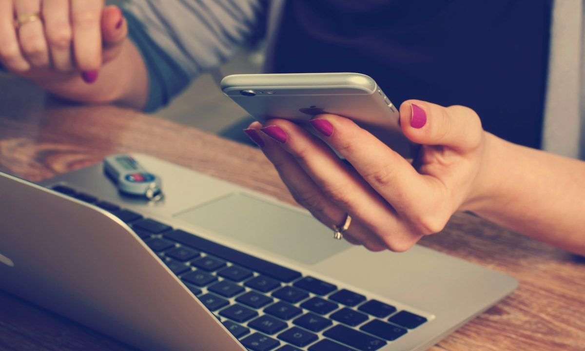 Persona con uno smartphone in mano davanti a un computer portatile.