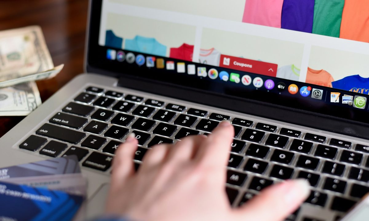 Persona che usa un portatile su una pagina di acquisti online, con carte e contanti in primo piano